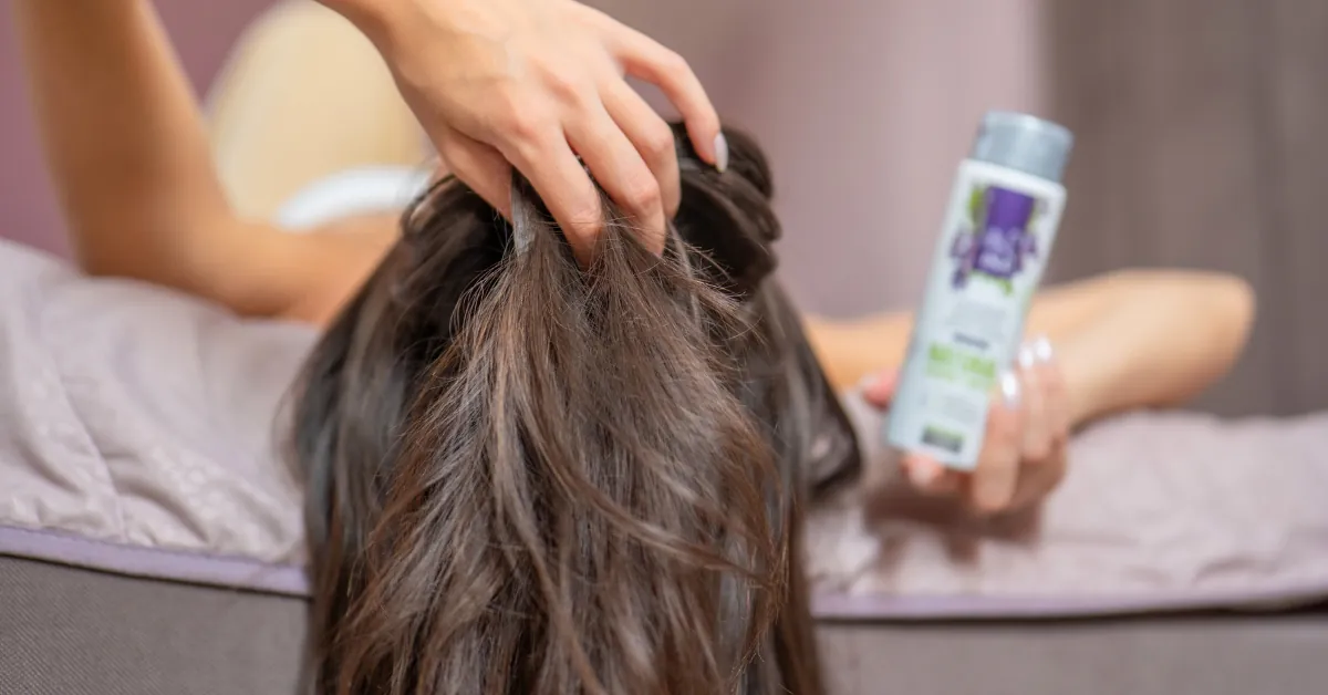 Donna che passa le dita tra i capelli per il prurito al cuoio capelluto senza forfora, accanto a lei l'Acqua alla Salvia Bio Hydrolina